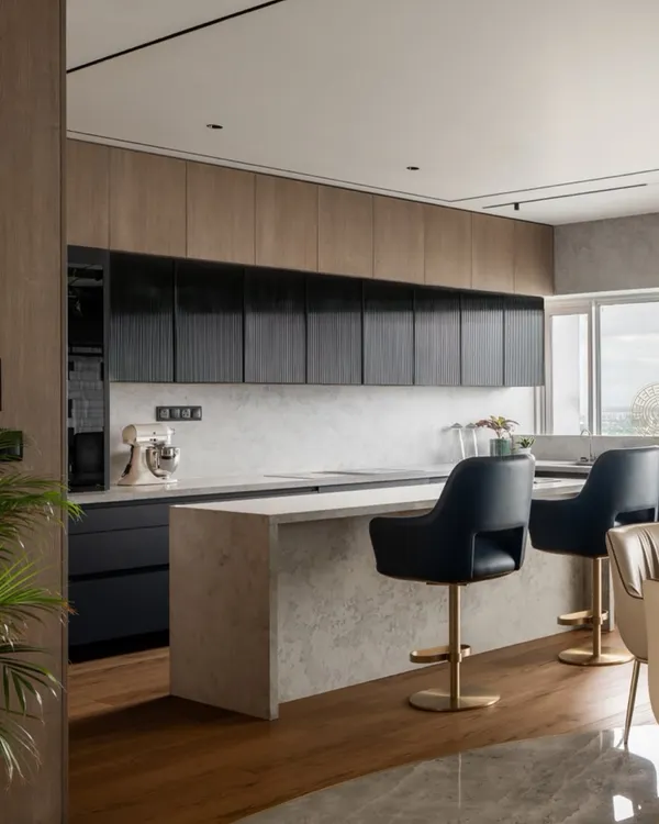 This show kitchen in our Kolkata project features a mix of wood and fluted black cabinetry for a modern, textured look. The large island with a stone finish provides ample workspace and seating, connecting the kitchen seamlessly to the living and dining areas.