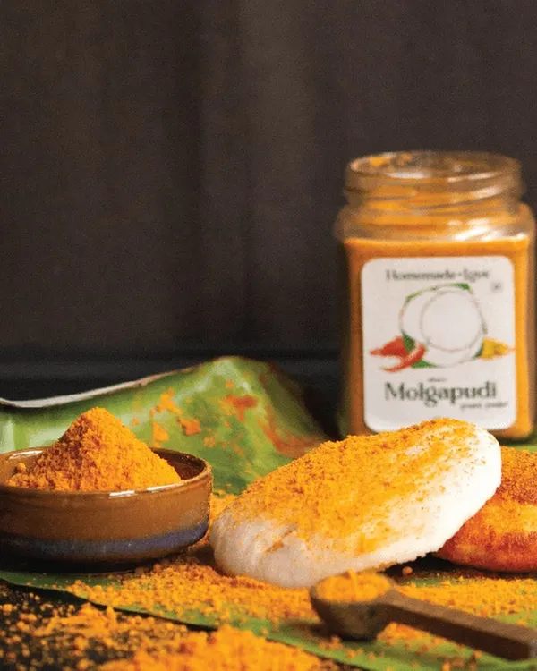 A classic South Indian breakfast scene featuring our authentic Molgapudi. This ground spice powder, served on a traditional banana leaf, is perfect for sprinkling over fluffy idlis, adding a burst of flavour and texture.