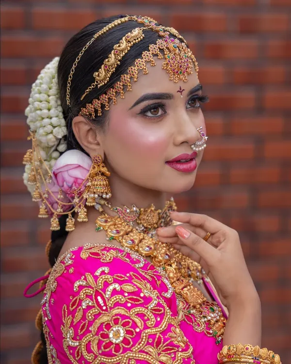 A close-up of a classic South Indian engagement look. The HD makeup provides a perfect canvas for the intricate temple jewellery, traditional matha patti, and a beautiful jasmine and rose braid.
