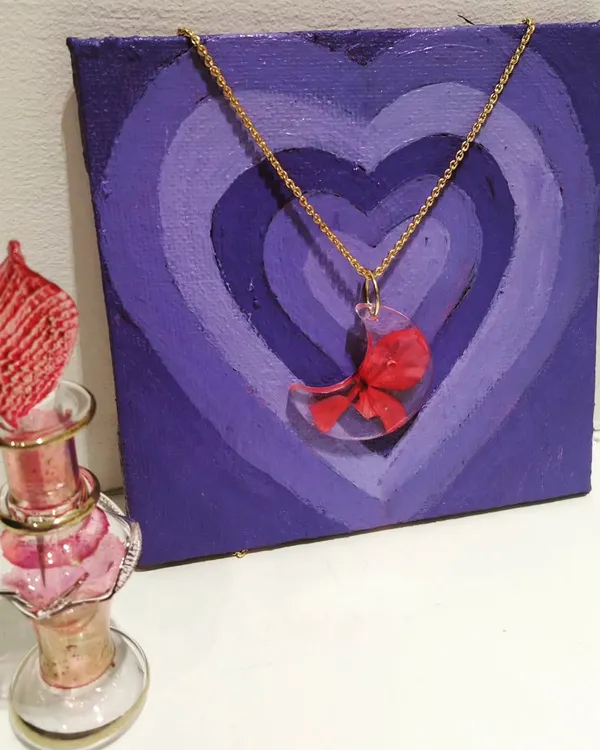 This crescent moon resin pendant holds a tiny, preserved red flower, hung on a delicate gold chain. It's a unique piece of wearable floral art.