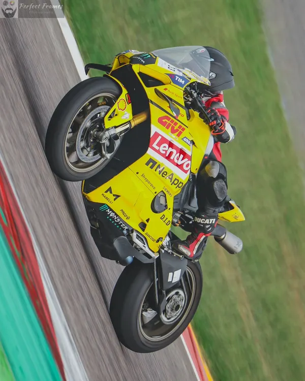 Power on display. A rider lifts the front wheel of a yellow Ducati Panigale, showing incredible control and confidence on the main straight at Buddh International Circuit.