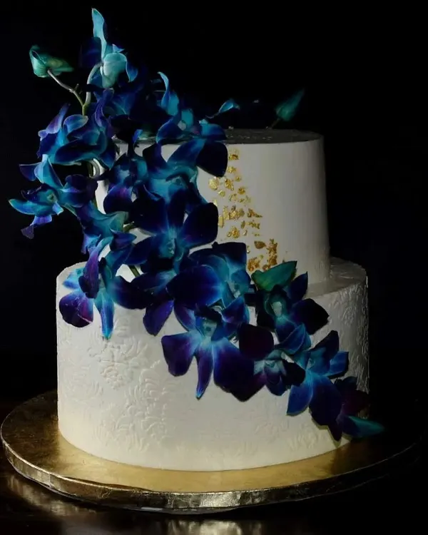 This two-tier red velvet cake is one of my favorites. The deep blue orchids cascading down the side create a dramatic and elegant look, complemented by delicate gold leaf accents and textured buttercream for a classy finish.
