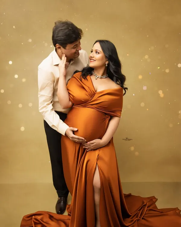 A glowing couple's portrait with a touch of magic. The mother-to-be looks radiant in a flowing rust-colored gown, complemented by sparkling light effects for a glamorous feel.