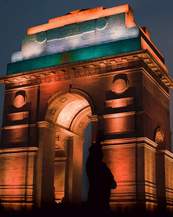 India Gate stands majestically, lit in the colors of the Indian flag, with the silhouette of the Amar Jawan Jyoti statue. This is a powerful, atmospheric shot that captures a sense of national pride.