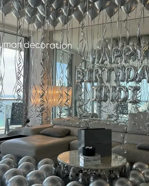A full room transformation for a birthday surprise. The space is filled with silver helium balloons on the ceiling and floor, with a "Happy Birthday" foil balloon banner as the centerpiece.