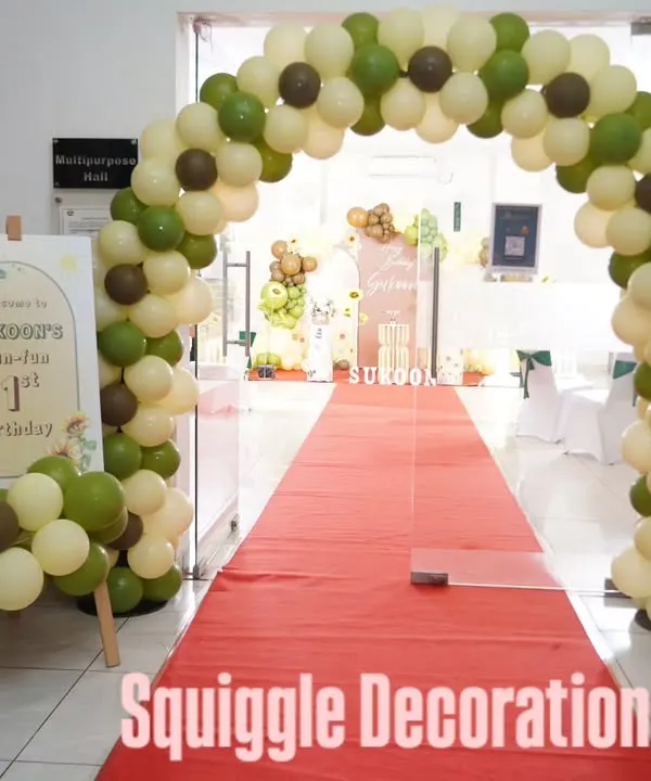 A grand entrance for a sunflower-themed party, featuring a red carpet and a beautiful balloon arch in olive green and cream.