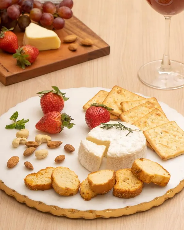 A styled shot of a cheese platter on an Ecstasy marble plate, paired with wine. This food styling demonstrates how to present serveware in an appealing, ready to use context for home goods brands.