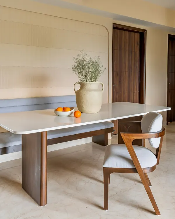 A modern dining nook from 'Project Lily,' featuring a sleek white-top table, a custom-built grey upholstered bench, and a stylish wooden dining chair. The textured wall adds warmth and depth.