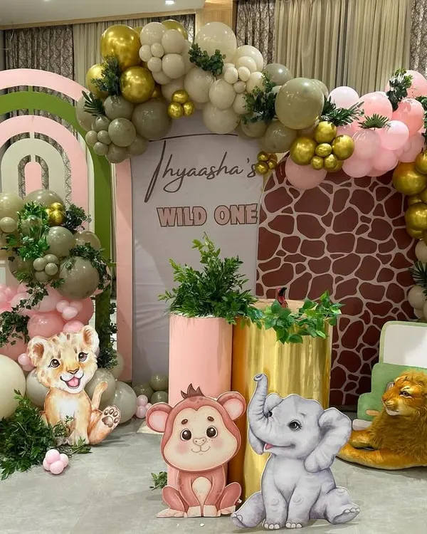 A vibrant and detailed 'Wild One' jungle theme birthday party. This setup features custom-designed backdrops with giraffe print, layered rainbow arches, and a variety of cute animal cutouts like a giraffe, lion, and elephant, creating a full safari experience for a first birthday.