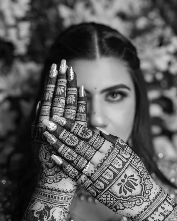 A black and white close-up that highlights the bold contrasts and intricate details of the henna. The lotus motif on the back of the hand is particularly striking in monochrome.