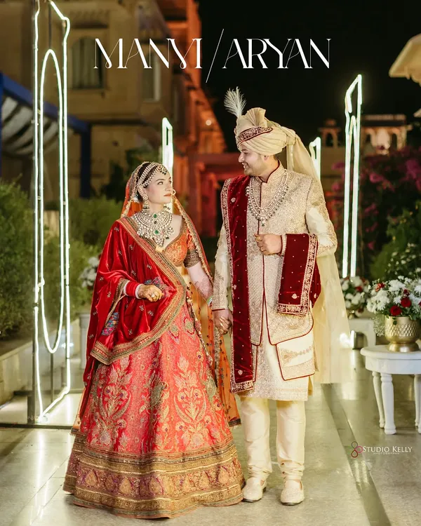 A royal couple portrait at night in Pushkar, with the groom in a classic sherwani and the bride in a traditional red lehenga, framed by the palace's illuminated archways.