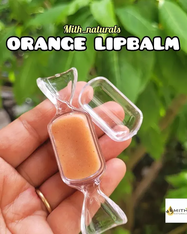 My homemade orange lip balm, shown here in its cute candy-shaped container. It's made to hydrate, heal chapped lips, and leave them feeling soft and moisturized.