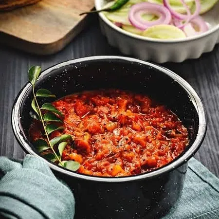 A bowl of my Yummy Fire Roasted Addictive Tomato Chutney, garnished with a fresh curry leaf. The fire-roasting process gives it a deep, smoky flavour.