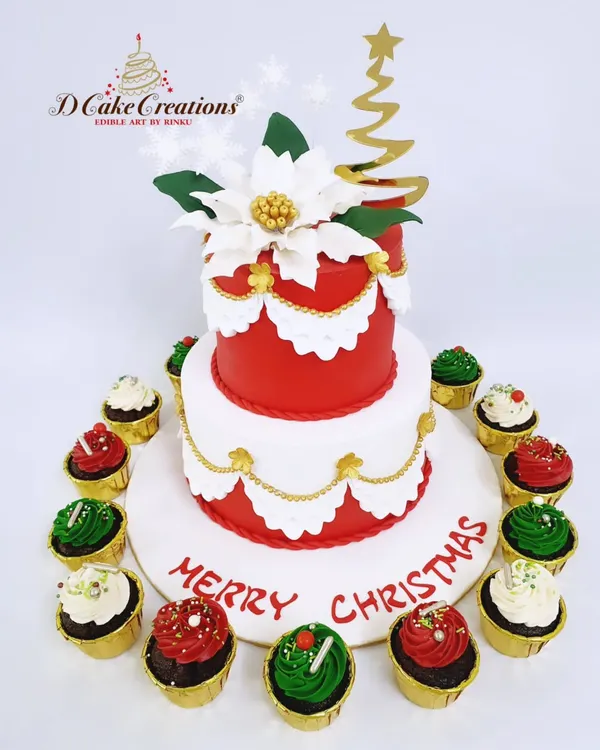 A festive two-tier Christmas cake, perfect for a holiday party centerpiece. This elegant creation features a red and white design with gold accents, a handmade sugar poinsettia, and is surrounded by matching red and green cupcakes.