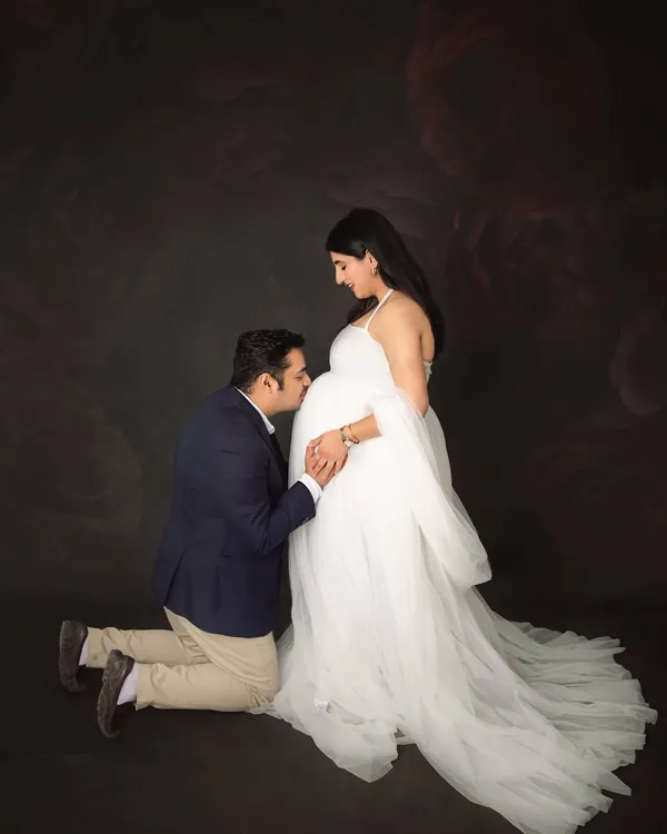 A classic and heartfelt pose. The dad-to-be kneels to kiss the baby bump, showing so much love and anticipation. The mom-to-be looks ethereal in a flowing white tulle gown.