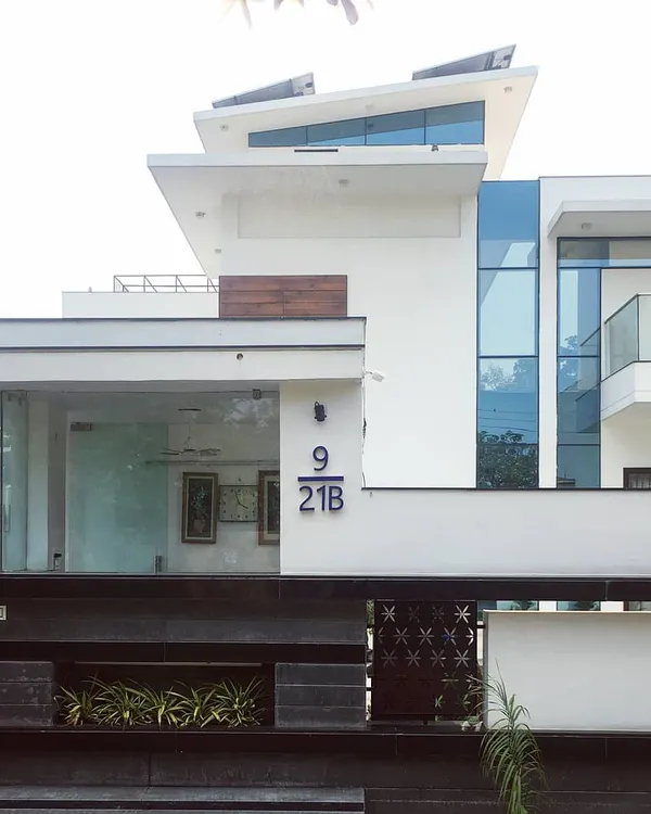 The contemporary exterior of Villa 9/21B, a private residence in Faridabad. The design is defined by its strong geometric lines, expansive glass panels, and a crisp white finish, creating a bold statement in modern residential architecture.