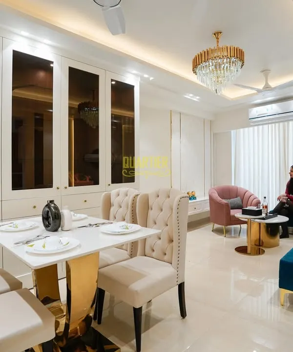 In this Tata Lavida, Gurugram home, I combined the living and dining areas into one cohesive, luxurious space. The design features a stunning crystal chandelier, plush tufted dining chairs, and a rich blue sofa, all tied together with elegant white and gold-accented cabinetry.