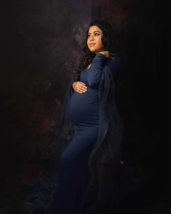 A portrait that feels like a painting. The deep blue gown and artistic lighting create a moody and powerfully elegant maternity photograph.