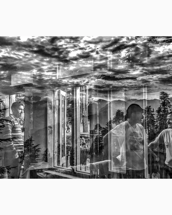 An in-camera reflection from Jibhi, Himachal Pradesh, blending the interior scene of people talking with the dramatic clouds and mountains outside. This black and white conceptual piece merges human interaction with the power of nature.