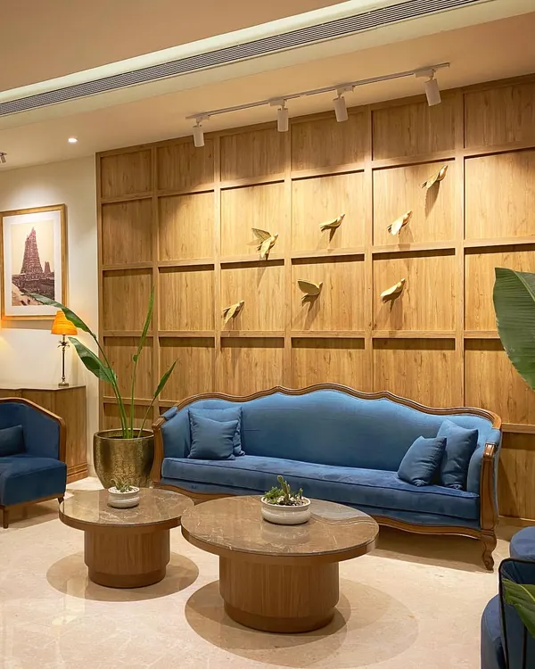 The completed entrance lobby at Keys Select Kattima, Chennai. The combination of classic blue sofas, warm wood paneling, and subtle metallic bird art creates a sophisticated yet comfortable waiting area for guests.