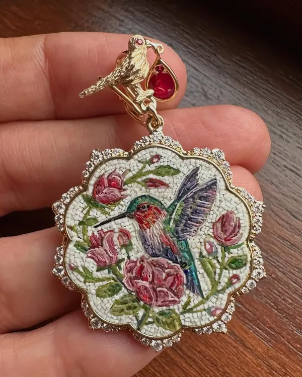 A close up of the hummingbird and roses pendant. You can see the individual tiles that form the image, a testament to the patient and detailed process of micromosaic art, all set with natural diamonds and a Mozambique ruby.
