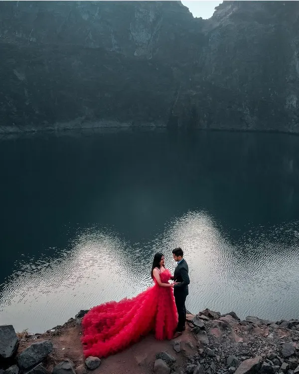 A dramatic portrait set against the vastness of nature. I believe love stories deserve epic backdrops, and this moment, with the vibrant red gown against the tranquil water, feels like a scene from a timeless romance.