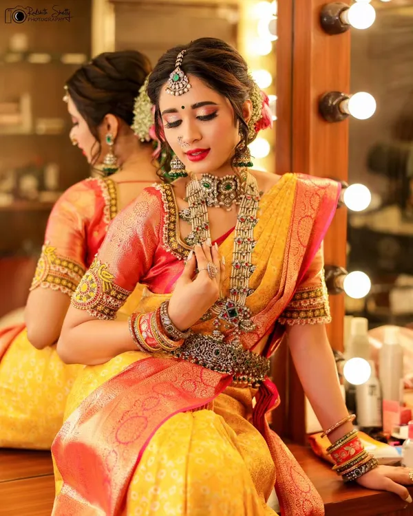 A beautiful moment of the bride at her vanity, surrounded by lights. This shot captures the final touches and the quiet anticipation before the main event, highlighting her stunning jewelry and makeup.