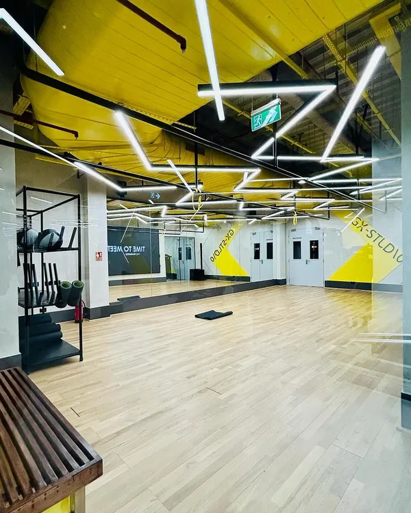 The group exercise studio at DLF Thrive in Chennai. The design features high-contrast yellow geometric patterns and dynamic overhead lighting on a wood-finish floor, creating a vibrant and motivating space for classes.