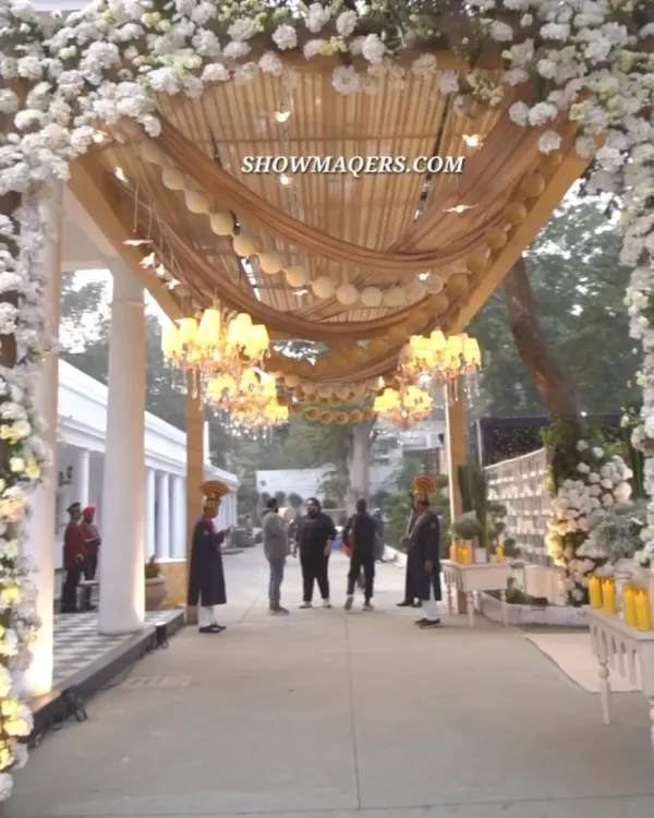 A grand entrance for an elegant Roka ceremony, featuring ivory drapes, lush white floral arches, and magnificent chandeliers. This design creates a luxurious and welcoming atmosphere for guests.