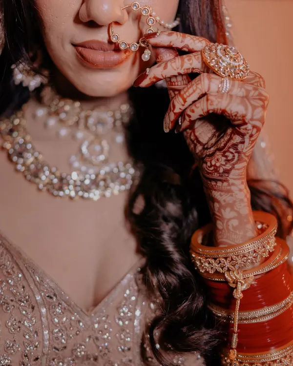 A close-up on the bride's hands, showcasing her beautiful bridal choora, intricate mehndi, and elegant nath. These details tell a story.