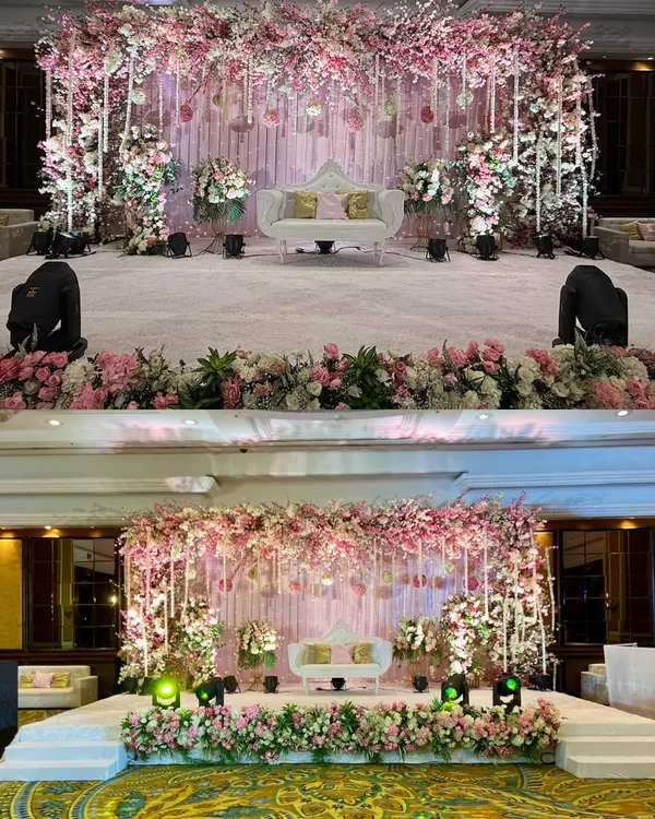 A dreamy pastel pink and white stage for a wedding reception. The cascading floral arch and delicate hanging details create a soft, romantic focal point for the couple.