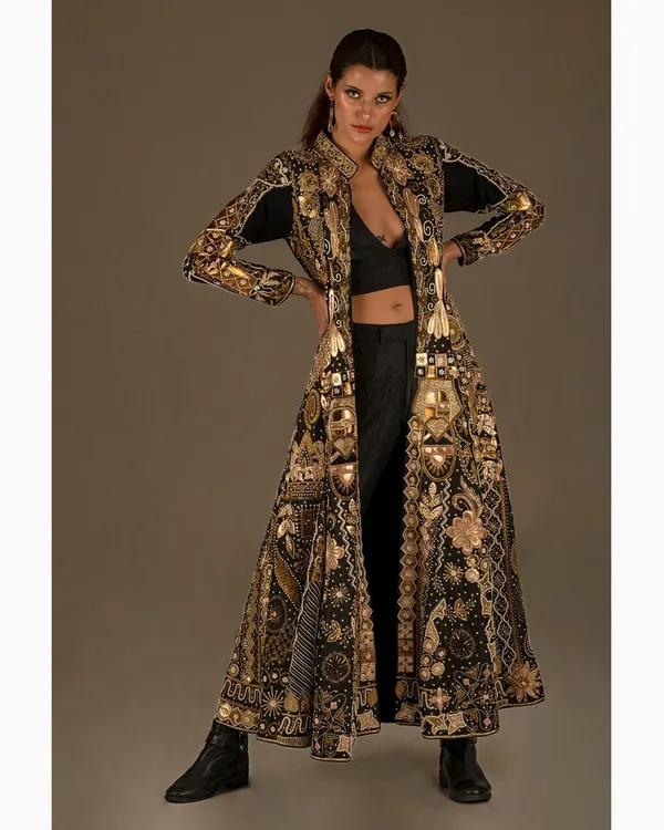 A high fashion studio portrait showcasing an intricate, floor-length coat by Nighat Izhar Designs. The powerful stance and dramatic lighting are central to this editorial look, blending traditional gold embroidery with a modern silhouette. This is an example of my conceptual fashion photography work.