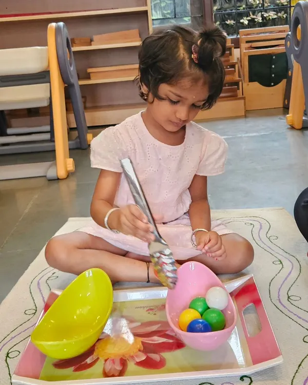A child carefully transfers items with a large spoon, an activity that develops fine motor skills, concentration, and coordination. These practical life exercises are the foundation of the Montessori method, preparing children for life.