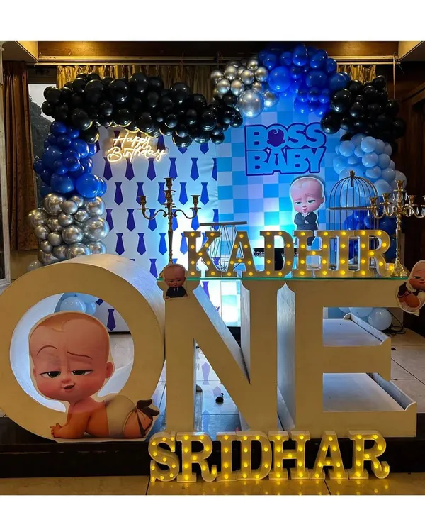 A complete Boss Baby themed first birthday stage. The setup features large "ONE" marquee letters, a custom backdrop with the movie's motifs, and a striking balloon arrangement in blue, black, and silver.