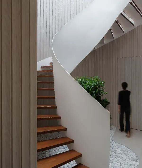 The helical staircase in the Hemadri penthouse is a central feature. Its swirling white form contrasts beautifully with the warm wood treads and the linear fluted wall, creating a dynamic yet elegant focal point.