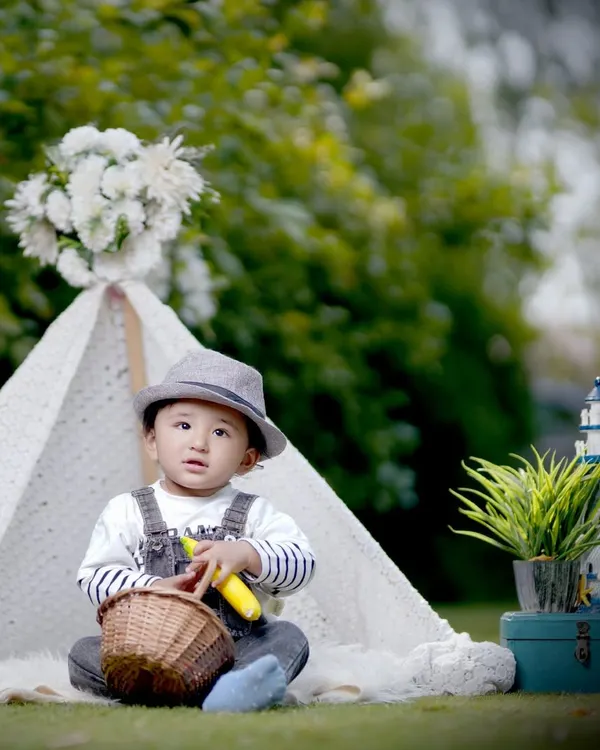 A professionally styled outdoor photoshoot for a toddler, featuring a lace teepee and rustic props in a green park setting. This is a great example of our themed kids' portrait sessions available in the Noida area.