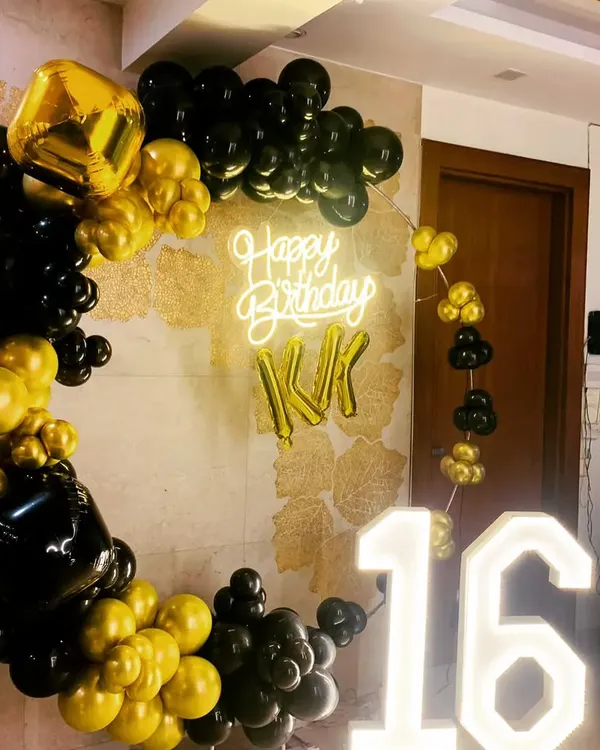 A sophisticated black and gold theme perfect for a sweet sixteen. This setup features a circular balloon arch, a "Happy Birthday" neon sign with the celebrant's initials, and large light-up marquee numbers for the age.
