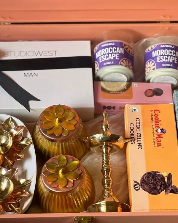A premium gift hamper for a man, featuring grooming products from Studio West, Moroccan Escape candles, and gourmet cookies. The elegant pink trunk and traditional brass lamp make it a sophisticated gift.