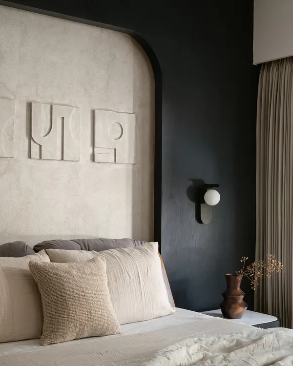 In this bedroom, I explored the power of a monochrome palette to create a space that is both youthful and sophisticated. The design is built on layers of texture, from the lime-washed wall behind the bed to the abstract art and soft linens. Every detail, including the modern wall sconce and custom headboard, was chosen to make the compact room feel intentional and full of character.