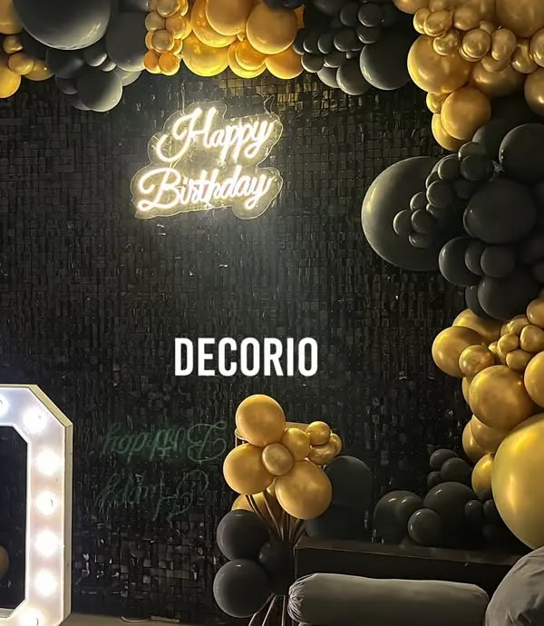 A surprise 50th birthday setup at home, featuring a bold black and gold theme. The decor includes a black sequin wall, a 'Happy Birthday' neon sign, and large '50' marquee numbers, transforming the living room into a stylish party space.