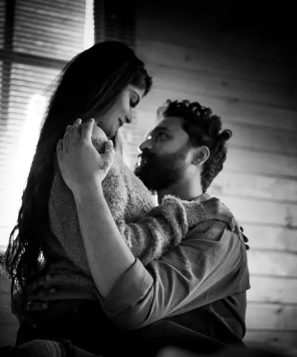 An intimate black and white portrait of a couple embracing. The dramatic lighting and their close connection create a powerful and emotional image that feels both timeless and deeply personal.