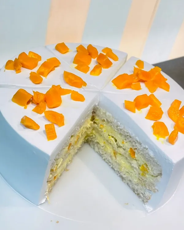 A slice taken from our fresh Mango Cake, revealing layers of light sponge and fresh mango pieces inside. A true taste of summer.