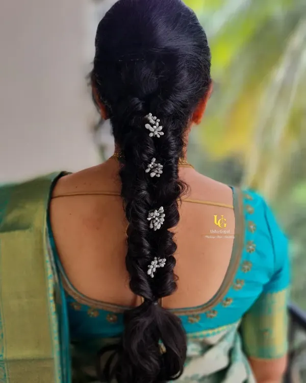 A classic and elegant hairstyle for a traditional event. This is a neatly twisted braid adorned with delicate, pearl-like floral accessories, perfect for a silk saree look.