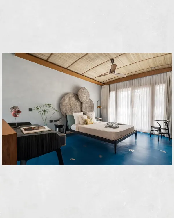 The master suite in the Kamala Residence is a study in texture. A ceiling of locally sourced banana fiber mats, blue oxide flooring, and a headboard made of distressed wood panels create a tropical, earthy ambiance.