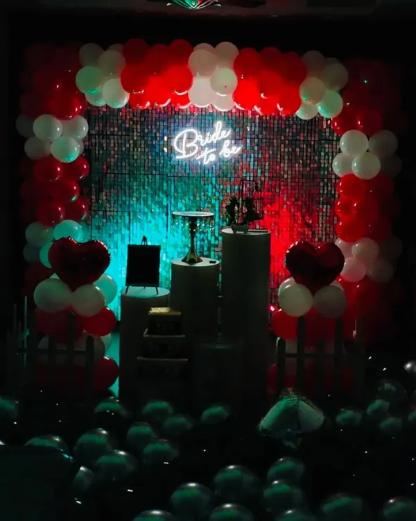 A "Bride to be" party setup seen in low light, where the neon sign and red accents truly pop. The dramatic lighting against the shimmer wall creates a chic and exciting atmosphere for the celebration.