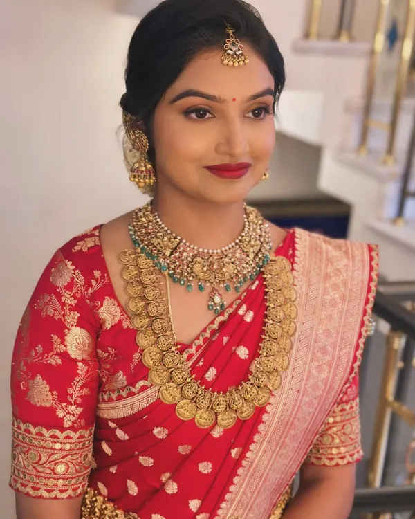 A close-up of Dr. Nayana's classic South Indian makeup look. The bright red lip and defined eyes pair perfectly with her traditional gold temple jewelry and red silk saree.