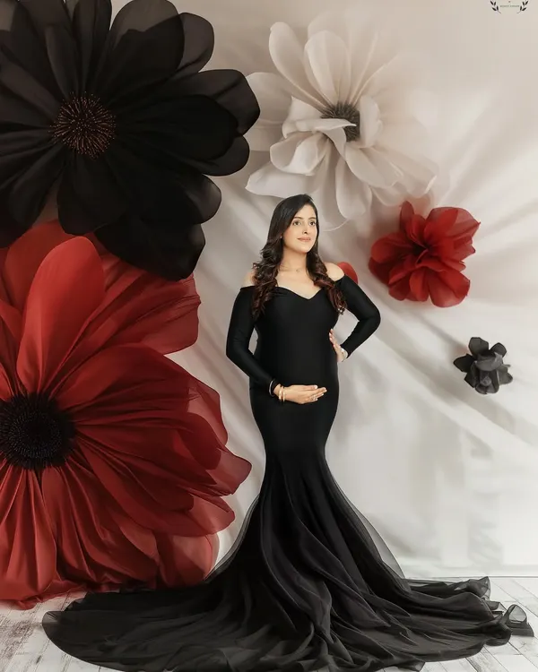 A portrait that feels like a piece of art. The expecting mother is framed by giant paper flowers, wearing an elegant black mermaid gown that beautifully highlights her form. This is a classic, dramatic maternity look.