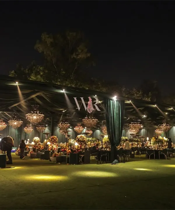 A spectacular wide view of an outdoor reception we designed. The entire space is enveloped in emerald green draping, with dozens of chandeliers creating a ceiling of light, transforming a simple lawn into a luxurious, otherworldly ballroom.