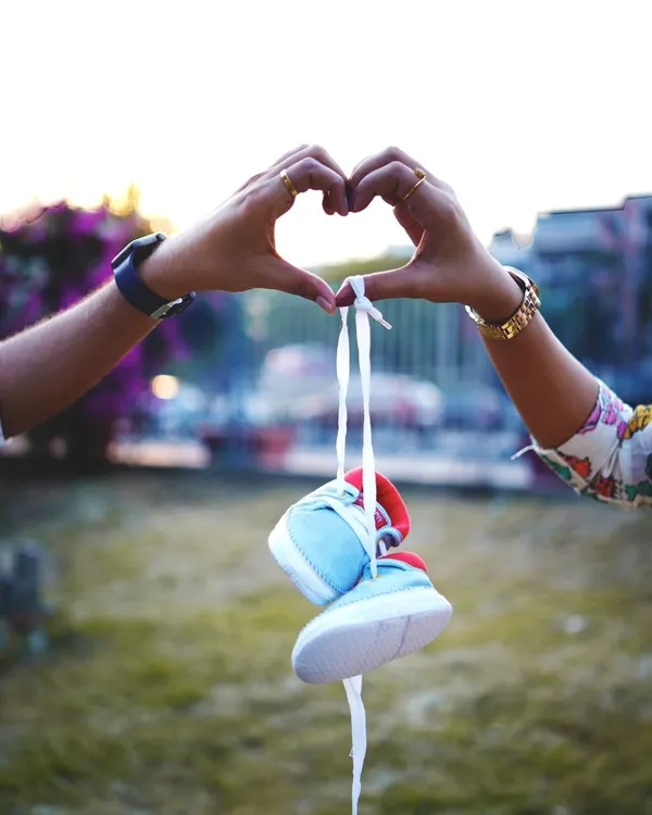 A classic and creative pregnancy announcement photo. The parents-to-be form a heart with their hands, holding a tiny pair of baby shoes, symbolizing their love and anticipation.