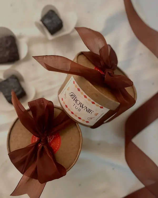Introducing our brownie tubs! A fudgy, eggless brownie drenched in rich chocolate sauce, elegantly packaged in a round tub with a ribbon. One spoonful and you’re hooked.
